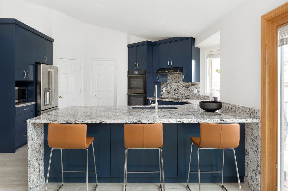 Inredning av ett modernt mellanstort flerfärgad flerfärgat kök, med en undermonterad diskho, släta luckor, blå skåp, granitbänkskiva, flerfärgad stänkskydd, rostfria vitvaror, laminatgolv, en halv köksö och grått golv
