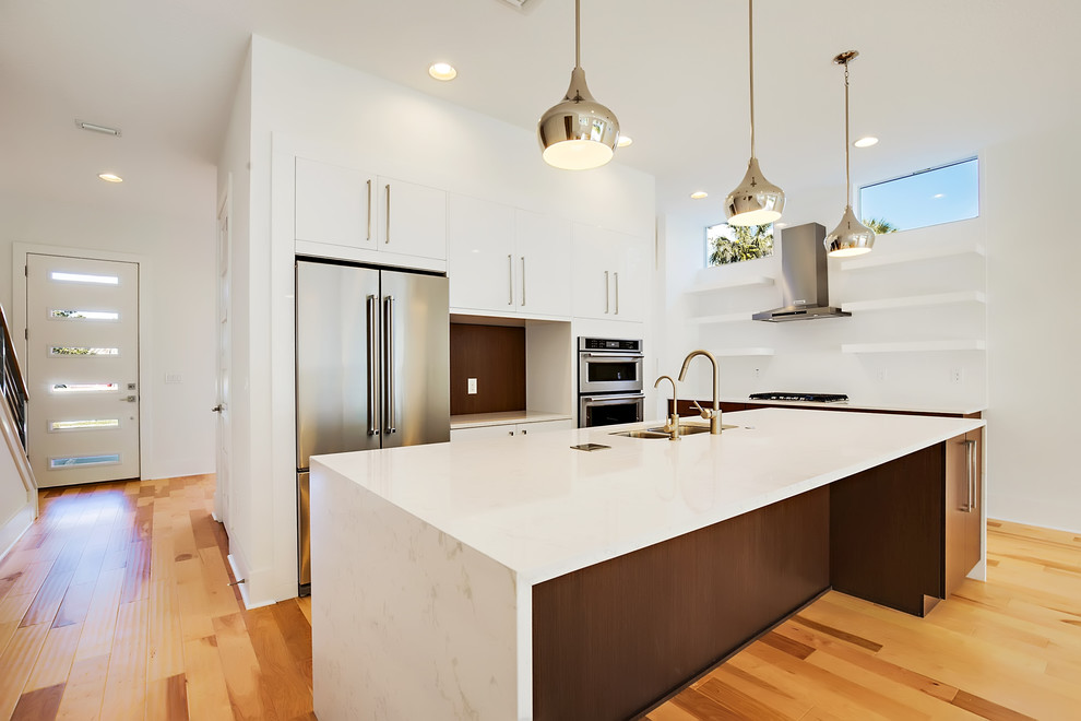 Inspiration for a modern open plan kitchen in Tampa with flat-panel cabinets, dark wood cabinets, engineered stone countertops, white splashback, ceramic splashback, stainless steel appliances, light hardwood flooring, an island, a submerged sink, beige floors and white worktops.