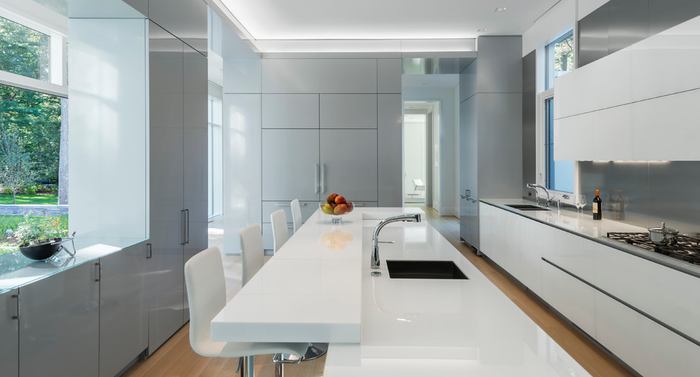 Moderne Küche in grau-weiß mit Doppelwaschbecken, flächenbündigen Schrankfronten, weißen Schränken, Küchenrückwand in Grau, Glasrückwand, hellem Holzboden und Kücheninsel in Boston
