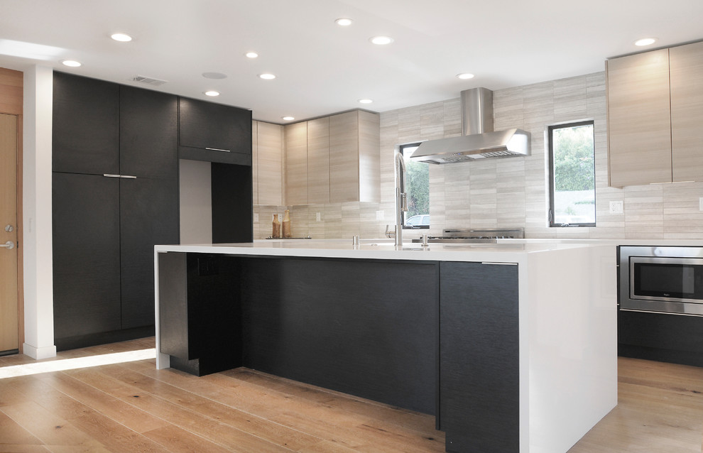 Example of a large minimalist l-shaped medium tone wood floor open concept kitchen design in San Diego with a single-bowl sink, flat-panel cabinets, black cabinets, quartz countertops, gray backsplash, subway tile backsplash, stainless steel appliances and an island