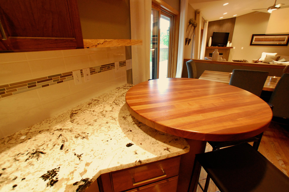 Inredning av ett modernt kök, med en undermonterad diskho, skåp i shakerstil, skåp i mörkt trä, granitbänkskiva, vitt stänkskydd, stänkskydd i tunnelbanekakel, rostfria vitvaror, ljust trägolv och en halv köksö