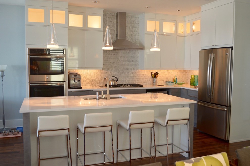 Foto på ett stort funkis kök, med en undermonterad diskho, släta luckor, vita skåp, bänkskiva i kvartsit, grått stänkskydd, stänkskydd i stenkakel, rostfria vitvaror, mellanmörkt trägolv och en köksö