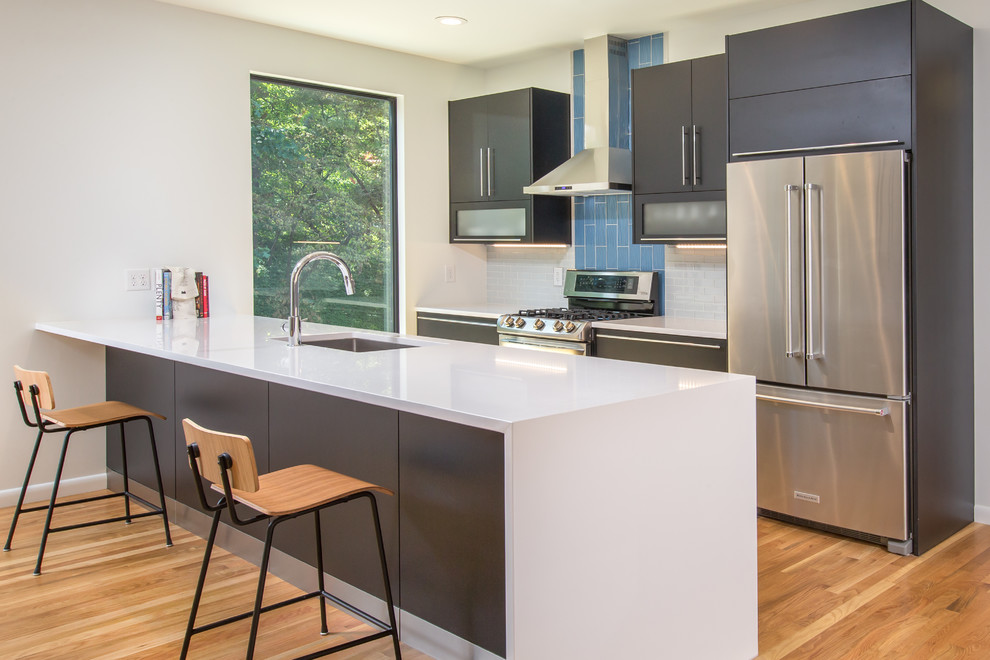 Bild på ett mellanstort funkis kök, med en undermonterad diskho, luckor med glaspanel, svarta skåp, bänkskiva i kvarts, blått stänkskydd, stänkskydd i glaskakel, rostfria vitvaror, ljust trägolv och en köksö