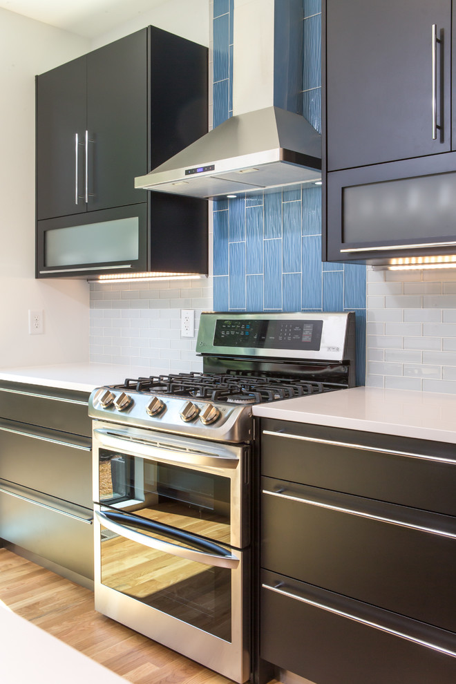Example of a mid-sized trendy galley light wood floor eat-in kitchen design in Other with an undermount sink, glass-front cabinets, black cabinets, quartz countertops, blue backsplash, glass tile backsplash, stainless steel appliances and an island