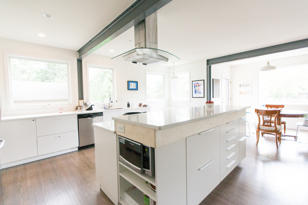 Large contemporary galley kitchen/diner in Minneapolis with a submerged sink, glass-front cabinets, white cabinets, engineered stone countertops, white splashback, stone slab splashback, stainless steel appliances, dark hardwood flooring and an island.