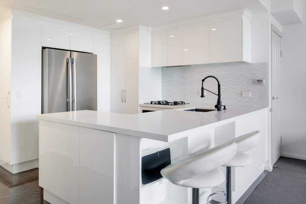 Idéer för ett litet modernt vit kök, med en undermonterad diskho, släta luckor, vita skåp, bänkskiva i kvarts, vitt stänkskydd, glaspanel som stänkskydd, rostfria vitvaror, klinkergolv i porslin, en halv köksö och brunt golv