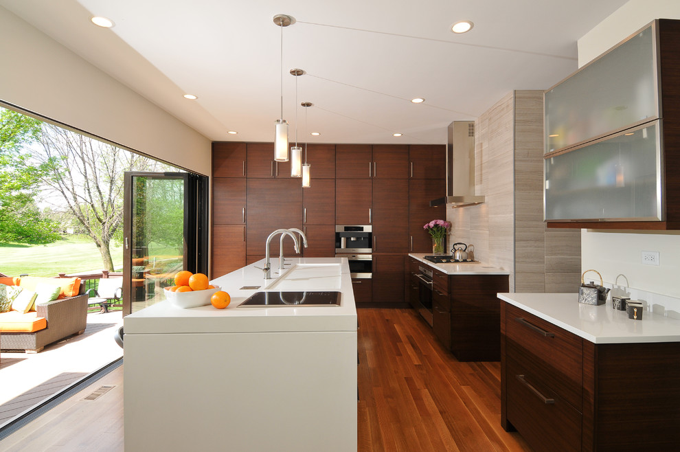 Photo of a medium sized contemporary l-shaped open plan kitchen in Chicago with flat-panel cabinets, dark wood cabinets, beige splashback, an island, an integrated sink, engineered stone countertops, integrated appliances, light hardwood flooring and stone tiled splashback.