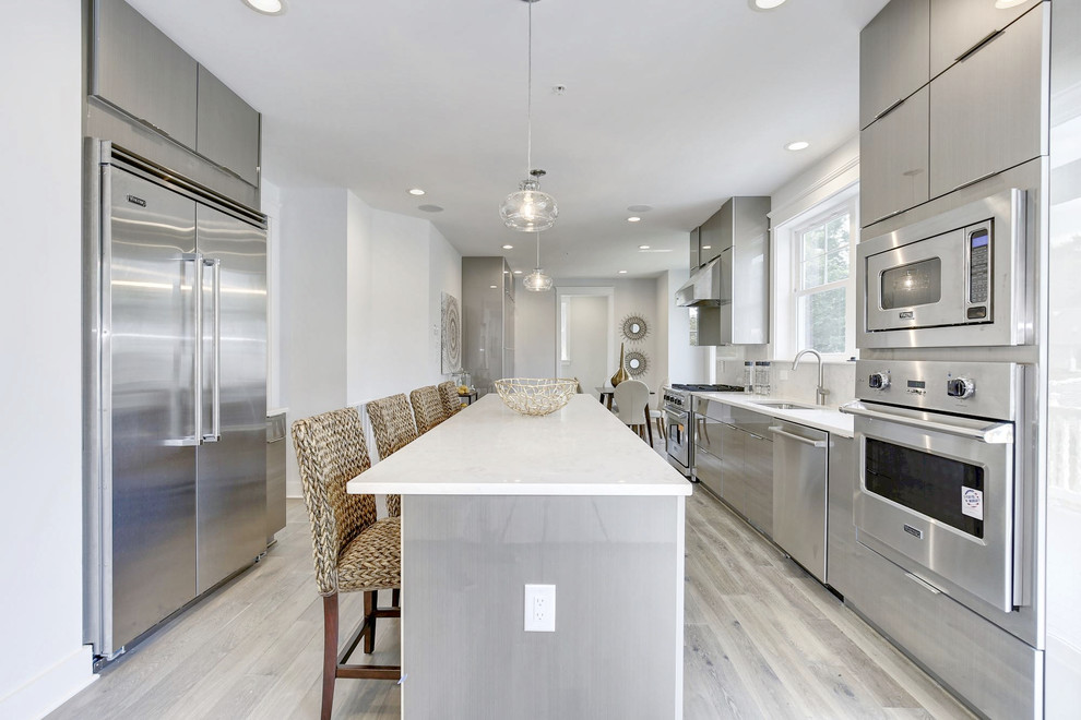 Immagine di una cucina moderna di medie dimensioni con lavello sottopiano, ante lisce, ante grigie, paraspruzzi multicolore, elettrodomestici in acciaio inossidabile, parquet chiaro, pavimento grigio e top bianco