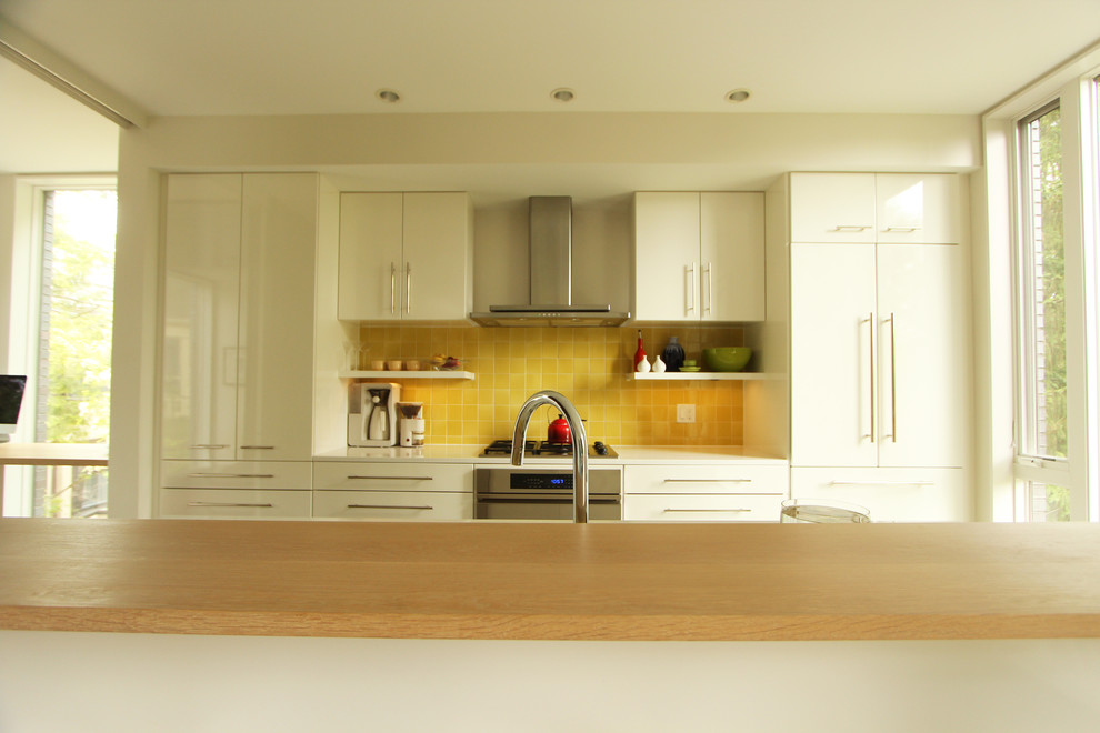 Modern inredning av ett litet linjärt kök med öppen planlösning, med en dubbel diskho, släta luckor, vita skåp, bänkskiva i kvarts, gult stänkskydd, stänkskydd i keramik, integrerade vitvaror, betonggolv och en köksö