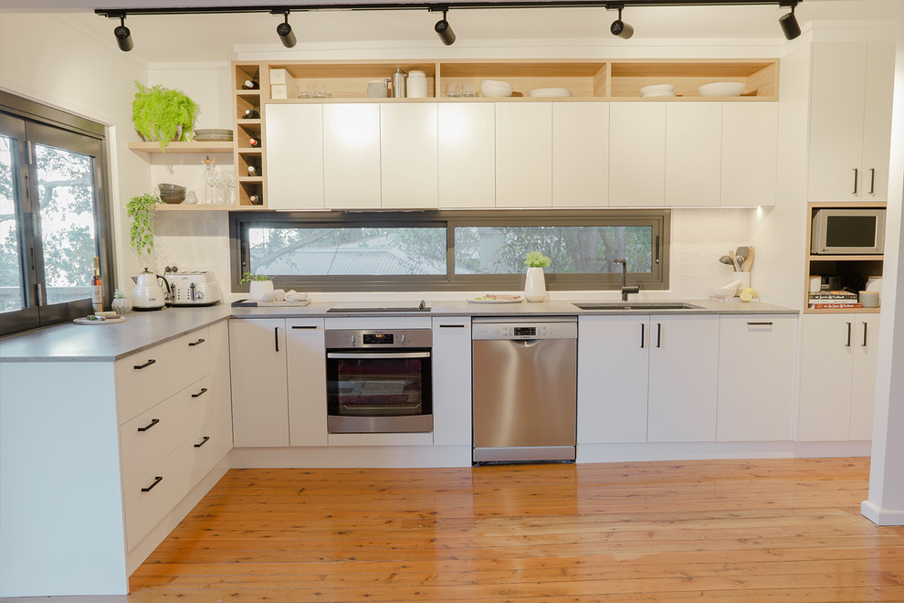 Idéer för mellanstora funkis grått kök, med en undermonterad diskho, släta luckor, vita skåp, bänkskiva i kvarts, grått stänkskydd, fönster som stänkskydd, rostfria vitvaror, ljust trägolv och orange golv