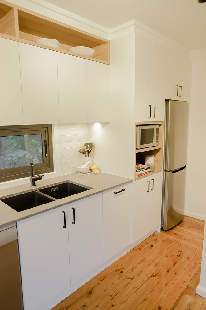 Bild på ett mellanstort funkis grå grått kök, med en undermonterad diskho, släta luckor, vita skåp, bänkskiva i kvarts, grått stänkskydd, fönster som stänkskydd, rostfria vitvaror, ljust trägolv och orange golv