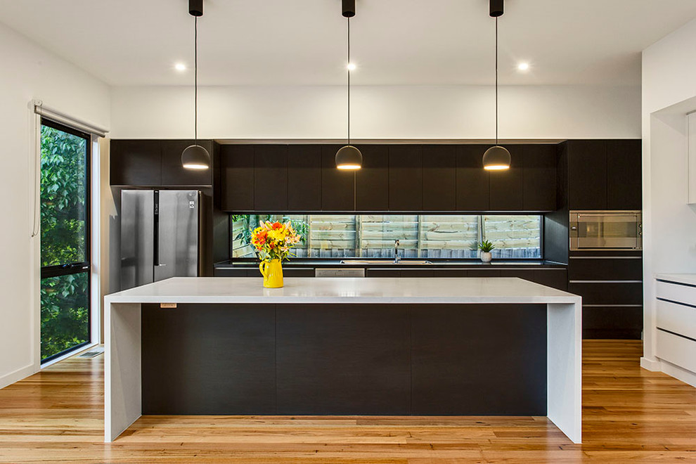 Moderne Küche mit flächenbündigen Schrankfronten, dunklen Holzschränken, Küchengeräten aus Edelstahl, braunem Holzboden und Kücheninsel in Melbourne