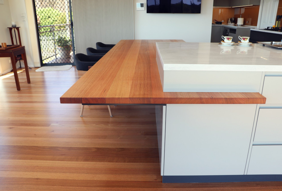 Photo of a large modern l-shaped open plan kitchen in Canberra - Queanbeyan with a double-bowl sink, flat-panel cabinets, grey cabinets, composite countertops, metallic splashback, glass sheet splashback, black appliances, medium hardwood flooring, multiple islands, multi-coloured floors and multicoloured worktops.