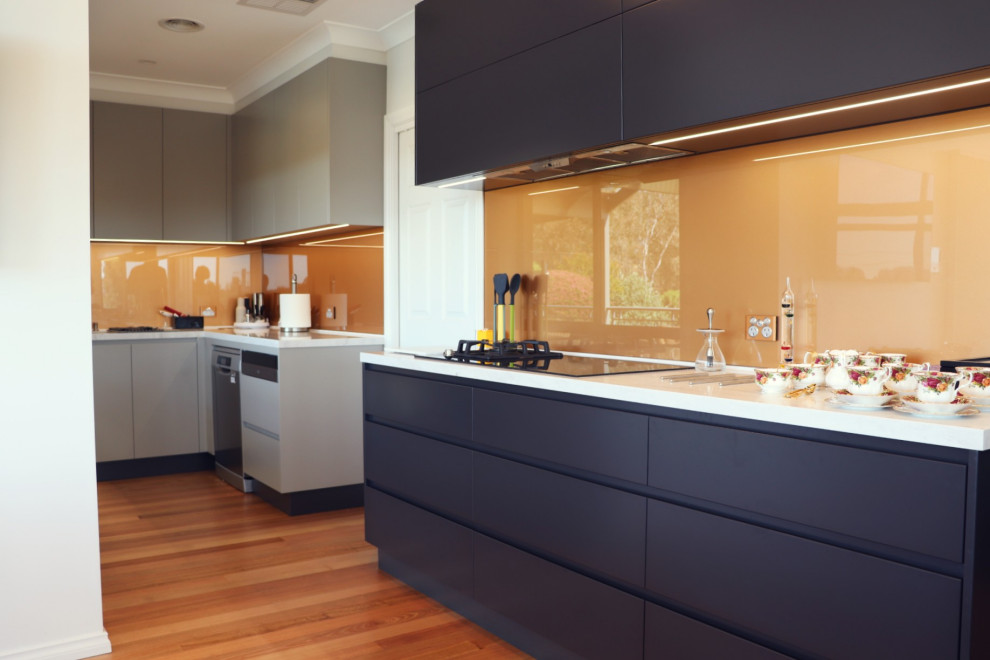 This is an example of a large modern l-shaped open plan kitchen in Canberra - Queanbeyan with a double-bowl sink, flat-panel cabinets, grey cabinets, composite countertops, metallic splashback, glass sheet splashback, black appliances, medium hardwood flooring, multiple islands, multi-coloured floors and multicoloured worktops.