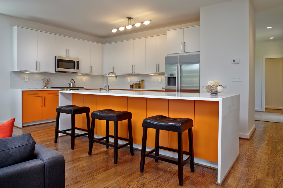 Bild på ett mellanstort funkis kök, med en undermonterad diskho, släta luckor, orange skåp, bänkskiva i kvarts, vitt stänkskydd, stänkskydd i tunnelbanekakel, rostfria vitvaror, mellanmörkt trägolv och en köksö