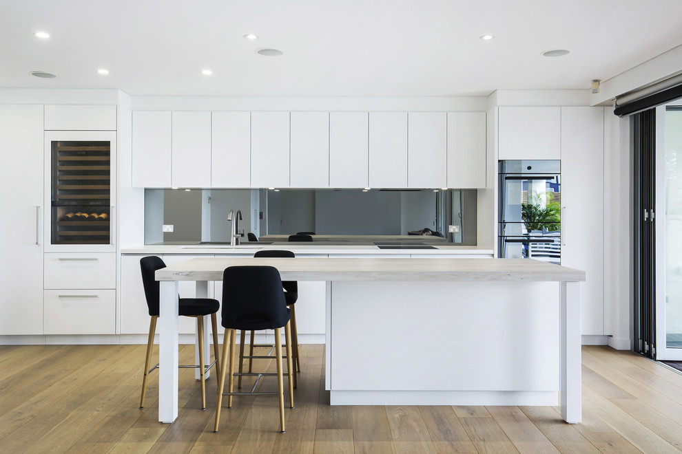 Inspiration for a contemporary single-wall kitchen in Sydney with a submerged sink, flat-panel cabinets, white cabinets, glass sheet splashback, light hardwood flooring, an island, brown floors and grey worktops.