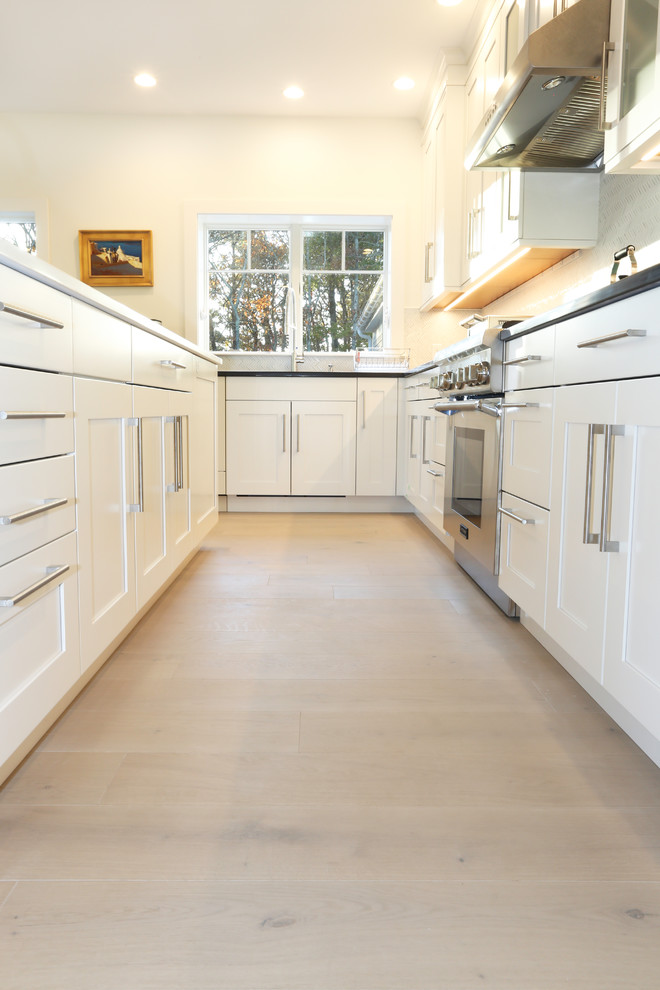 Example of a mid-sized minimalist galley light wood floor and gray floor open concept kitchen design in Boston with white cabinets, stainless steel appliances and an island