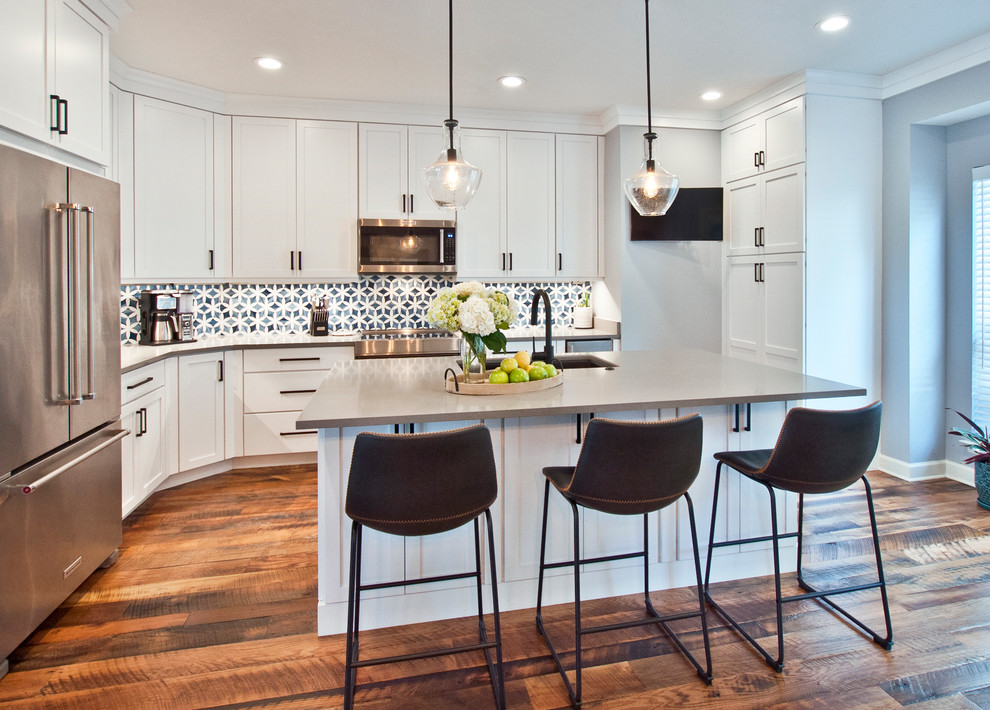 Example of a mid-sized transitional l-shaped medium tone wood floor and brown floor enclosed kitchen design in Nashville with an undermount sink, shaker cabinets, white cabinets, quartz countertops, multicolored backsplash, stainless steel appliances, an island, gray countertops and mosaic tile backsplash