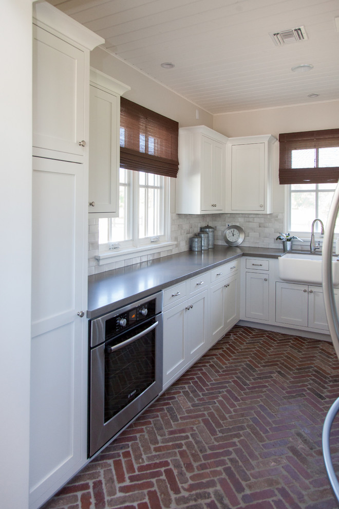 Large classic u-shaped kitchen in Phoenix with a belfast sink, white cabinets, stainless steel worktops, brick flooring and shaker cabinets.