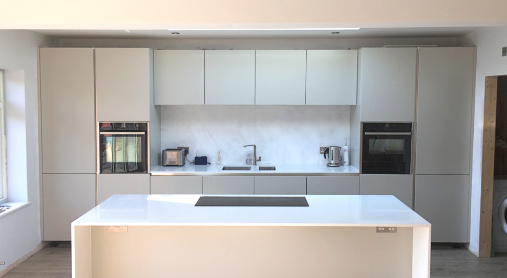 Bild på ett mellanstort funkis vit vitt kök, med en undermonterad diskho, grå skåp, bänkskiva i kvartsit, stänkskydd med metallisk yta, glaspanel som stänkskydd, svarta vitvaror, laminatgolv, en köksö och brunt golv