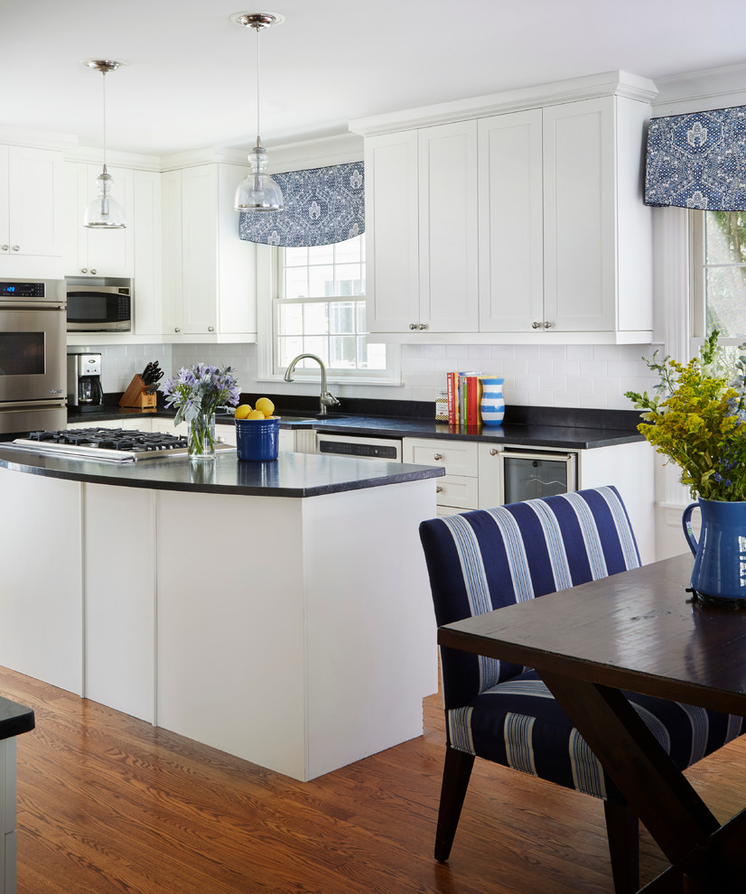 This is an example of a large beach style l-shaped kitchen/diner in Chicago with a submerged sink, shaker cabinets, white cabinets, soapstone worktops, white splashback, metro tiled splashback, stainless steel appliances, dark hardwood flooring, an island, brown floors and black worktops.