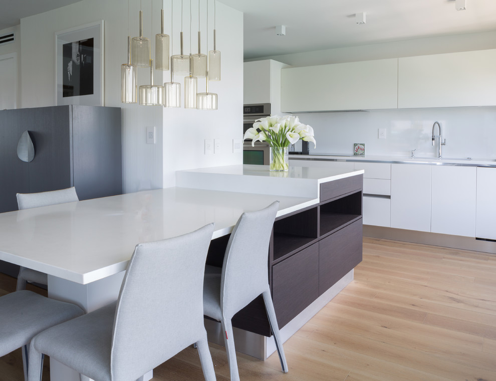 Immagine di una cucina minimal di medie dimensioni con ante di vetro, ante bianche, top in quarzo composito, paraspruzzi bianco e pavimento in legno massello medio