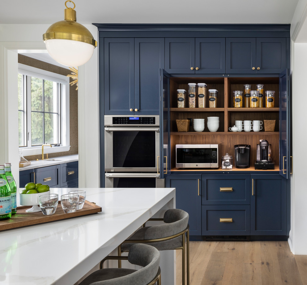 Foto på ett stort funkis vit kök, med en undermonterad diskho, skåp i shakerstil, blå skåp, bänkskiva i kvarts, vitt stänkskydd, integrerade vitvaror, ljust trägolv, en köksö och brunt golv