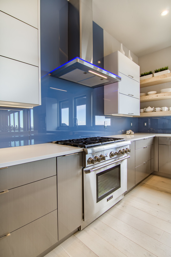 Expansive modern u-shaped open plan kitchen in Other with a belfast sink, flat-panel cabinets, grey cabinets, engineered stone countertops, blue splashback, glass sheet splashback, stainless steel appliances, light hardwood flooring, an island and beige floors.