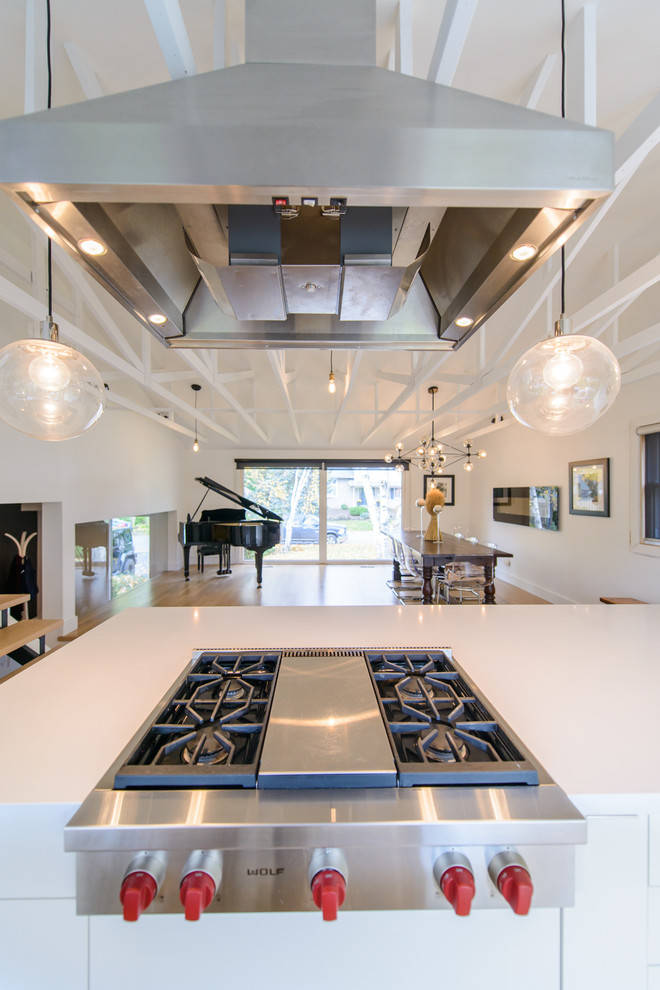 This is an example of an expansive contemporary galley open plan kitchen in Toronto with an island, flat-panel cabinets, white cabinets, stainless steel appliances, a built-in sink and medium hardwood flooring.