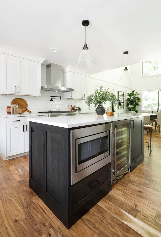 Exempel på ett mellanstort lantligt vit vitt kök, med en undermonterad diskho, skåp i shakerstil, vita skåp, bänkskiva i kvarts, vitt stänkskydd, stänkskydd i keramik, rostfria vitvaror, mellanmörkt trägolv, en köksö och brunt golv
