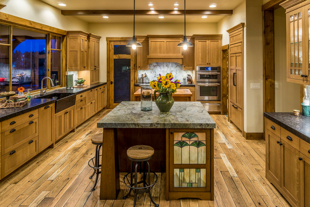 Large mountain style u-shaped medium tone wood floor and brown floor enclosed kitchen photo in Other with a farmhouse sink, shaker cabinets, medium tone wood cabinets, soapstone countertops, multicolored backsplash, stone slab backsplash, paneled appliances, two islands and black countertops