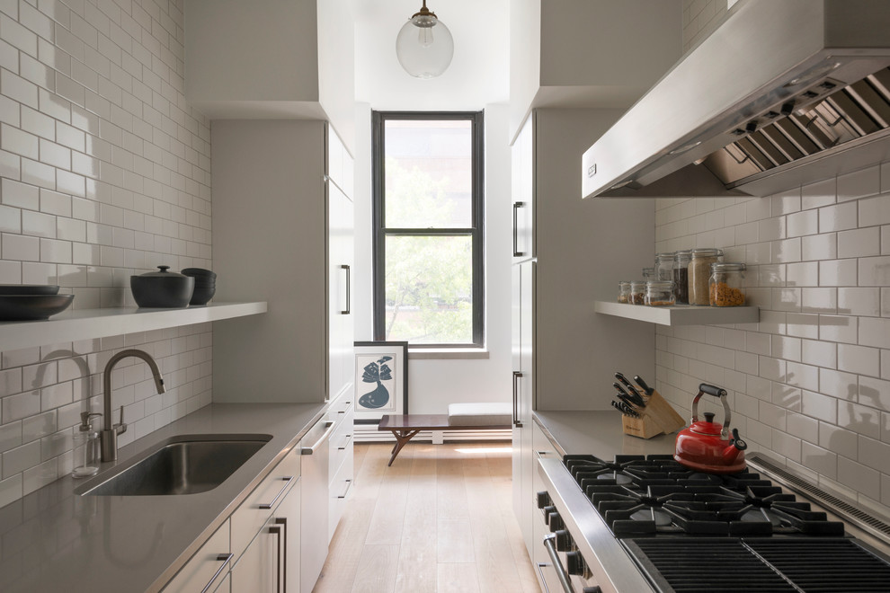 Réalisation d'une cuisine parallèle nordique fermée avec un évier encastré, un placard à porte plane, des portes de placard blanches, un plan de travail en inox, une crédence blanche, une crédence en carrelage métro, un électroménager en acier inoxydable, parquet clair et aucun îlot.