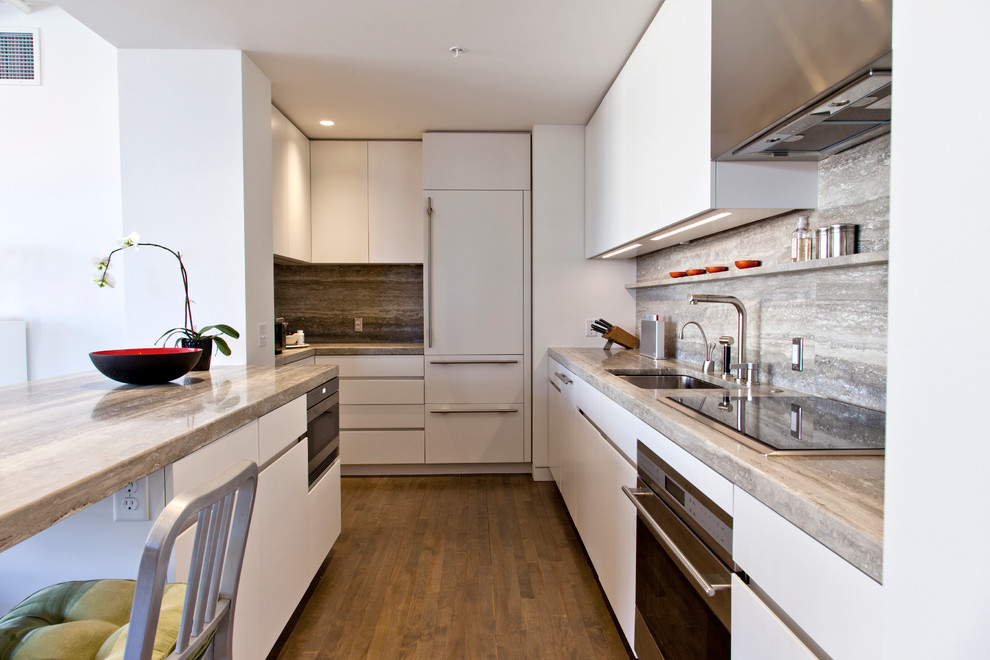 Modern inredning av ett avskilt u-kök, med en undermonterad diskho, släta luckor, vita skåp, grått stänkskydd, integrerade vitvaror och stänkskydd i travertin