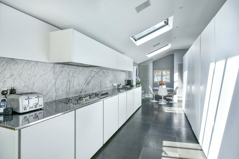 Inspiration for a modern kitchen/diner in London with an integrated sink, flat-panel cabinets, white cabinets, stainless steel worktops, white splashback, marble splashback, no island and grey floors.