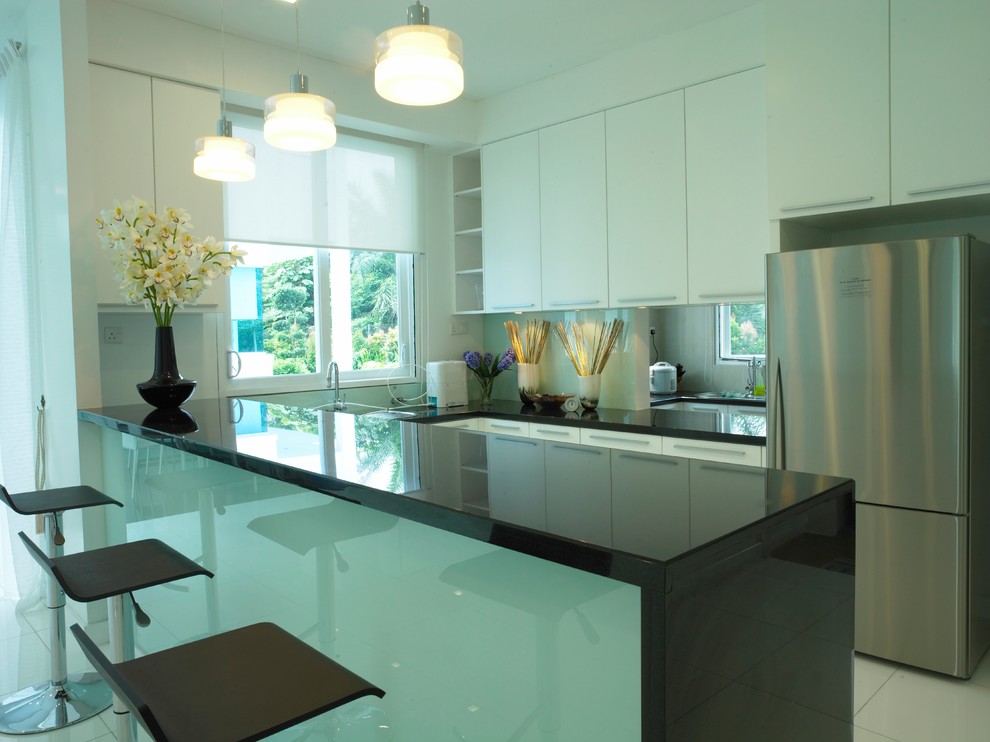This is an example of a medium sized modern u-shaped kitchen/diner in Other with a single-bowl sink, flat-panel cabinets, white cabinets, quartz worktops, green splashback, glass sheet splashback, stainless steel appliances, marble flooring, an island, white floors and black worktops.