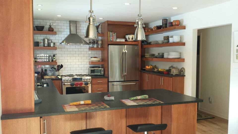 Inredning av ett modernt kök, med en undermonterad diskho, öppna hyllor, skåp i mellenmörkt trä, granitbänkskiva, vitt stänkskydd, stänkskydd i tunnelbanekakel, rostfria vitvaror, ljust trägolv och en halv köksö