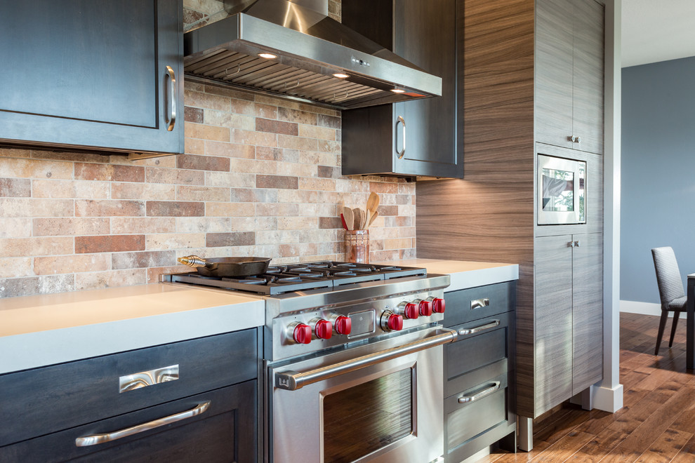 ポートランドにある広いおしゃれなキッチン (エプロンフロントシンク、落し込みパネル扉のキャビネット、濃色木目調キャビネット、茶色いキッチンパネル、シルバーの調理設備、無垢フローリング、茶色い床) の写真