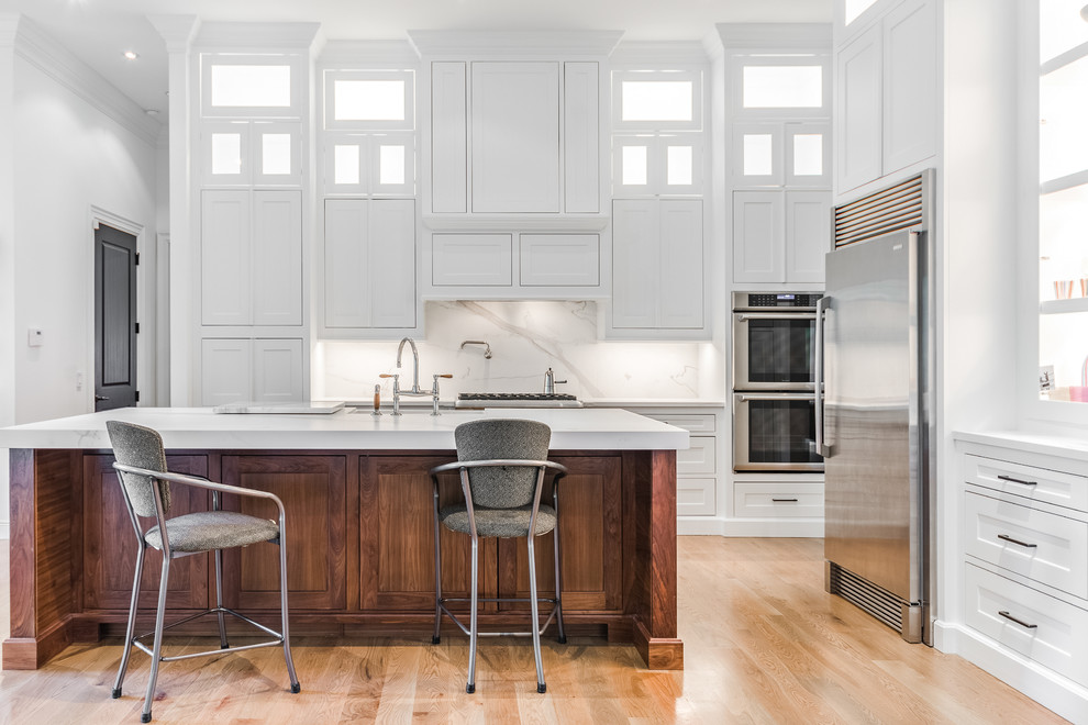 Example of a mid-sized single-wall light wood floor and brown floor eat-in kitchen design in Other with shaker cabinets, white cabinets, white backsplash, stainless steel appliances, a peninsula and white countertops