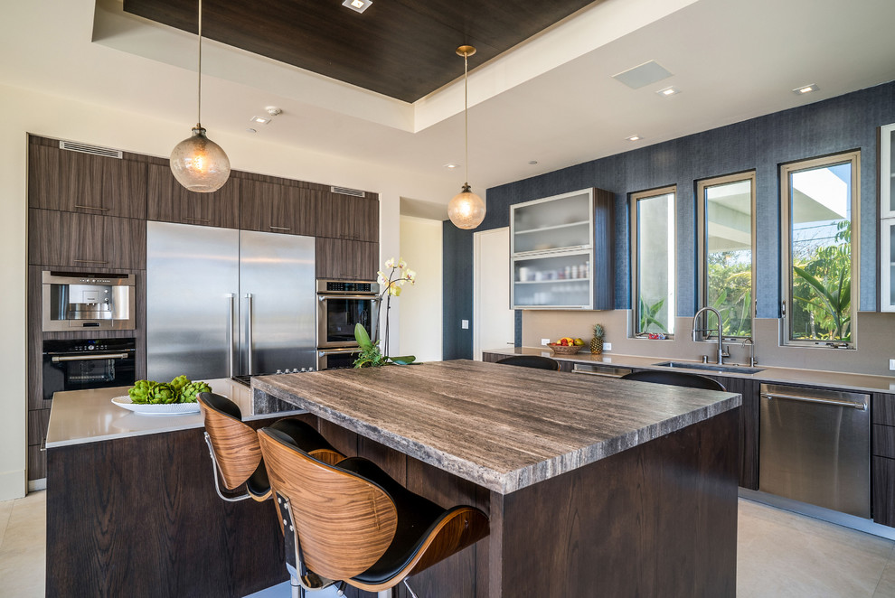 Inspiration for a large coastal l-shaped travertine floor open concept kitchen remodel in Los Angeles with an undermount sink, flat-panel cabinets, medium tone wood cabinets, solid surface countertops, beige backsplash, stainless steel appliances, two islands and beige countertops