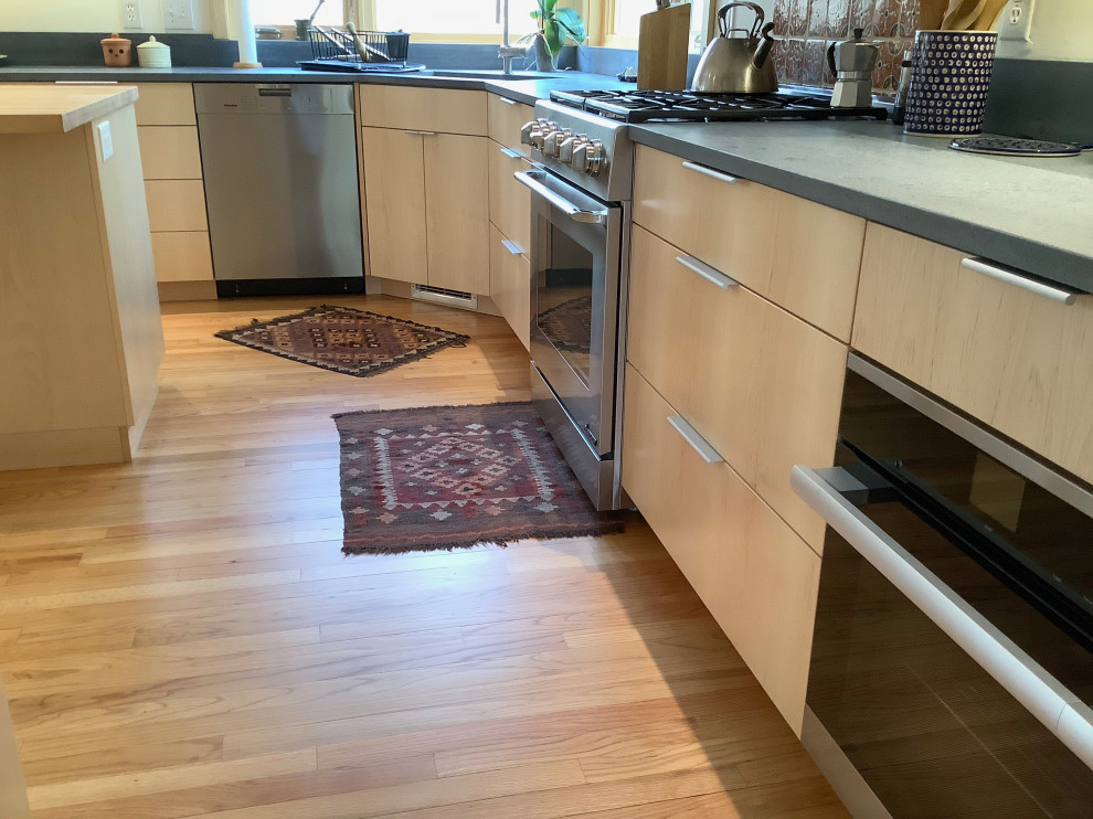 Bild på ett stort funkis grå grått kök, med en undermonterad diskho, släta luckor, skåp i ljust trä, bänkskiva i täljsten, rött stänkskydd, stänkskydd i keramik, rostfria vitvaror, kalkstensgolv, en köksö och beiget golv