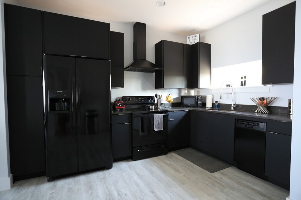 Foto på ett mellanstort funkis kök, med en dubbel diskho, släta luckor, svarta skåp, bänkskiva i kvarts, svart stänkskydd, svarta vitvaror, ljust trägolv och vitt golv
