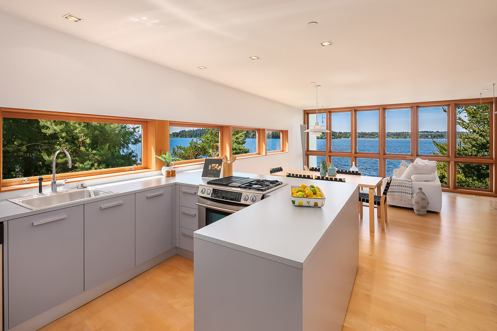 Exempel på ett mellanstort maritimt grå grått kök, med en nedsänkt diskho, grå skåp, orange golv, släta luckor, fönster som stänkskydd, rostfria vitvaror, mellanmörkt trägolv och en halv köksö