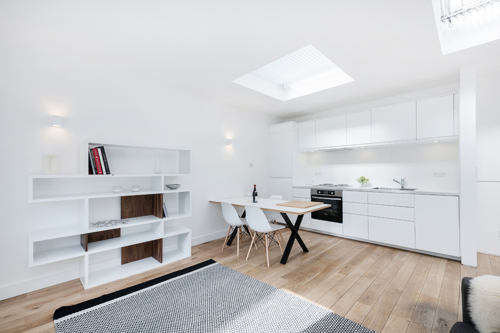 Small contemporary single-wall open plan kitchen in London with a double-bowl sink, flat-panel cabinets, white cabinets, laminate countertops, white splashback, ceramic splashback, stainless steel appliances, light hardwood flooring and no island.