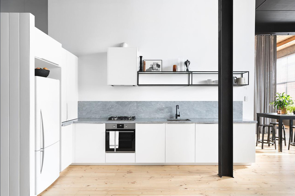 Moderne Küche in L-Form mit Unterbauwaschbecken, flächenbündigen Schrankfronten, weißen Schränken, Küchenrückwand in Grau, hellem Holzboden, Halbinsel, beigem Boden und grauer Arbeitsplatte in Melbourne