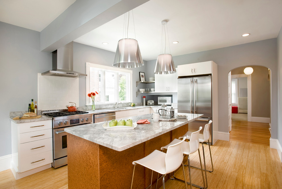 Example of a mid-sized trendy l-shaped light wood floor eat-in kitchen design in Boston with stainless steel appliances, an undermount sink, white cabinets, granite countertops, an island, flat-panel cabinets, white backsplash and ceramic backsplash