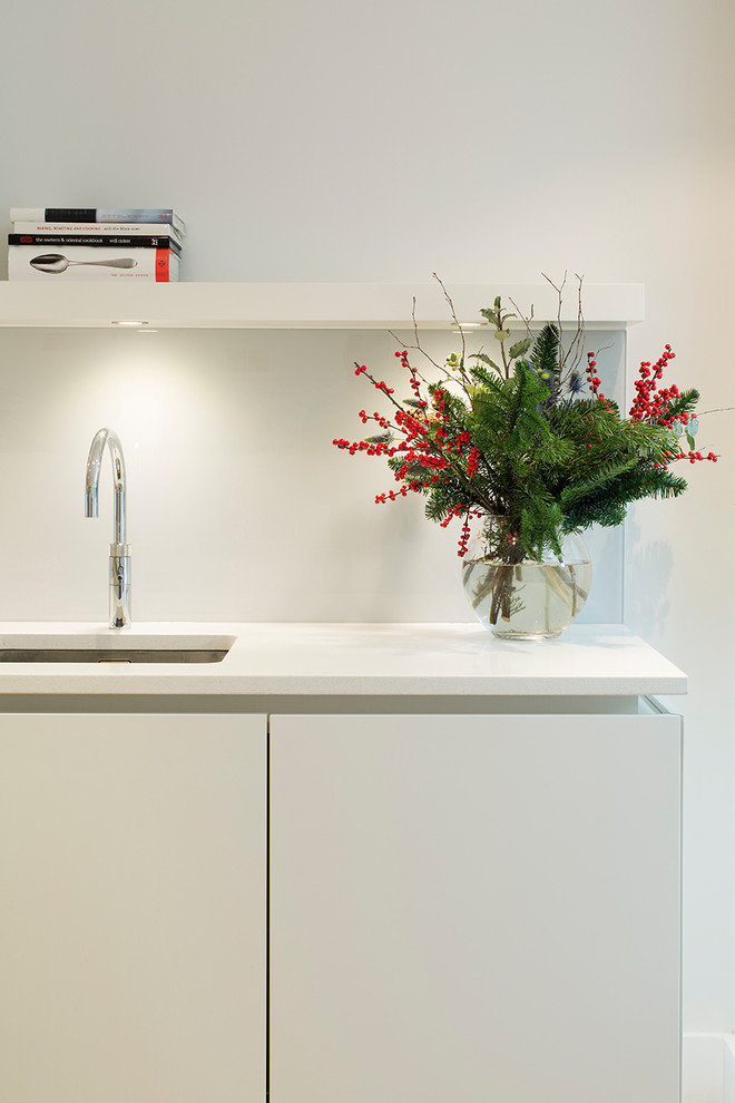 Inspiration for a large contemporary single-wall open plan kitchen in London with a built-in sink, flat-panel cabinets, white cabinets, quartz worktops, grey splashback, glass sheet splashback, stainless steel appliances, light hardwood flooring and an island.