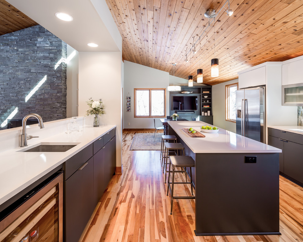 Mittelgroße Moderne Wohnküche in L-Form mit flächenbündigen Schrankfronten, grauen Schränken, Quarzwerkstein-Arbeitsplatte, Glasrückwand, Küchengeräten aus Edelstahl, hellem Holzboden und zwei Kücheninseln in Minneapolis