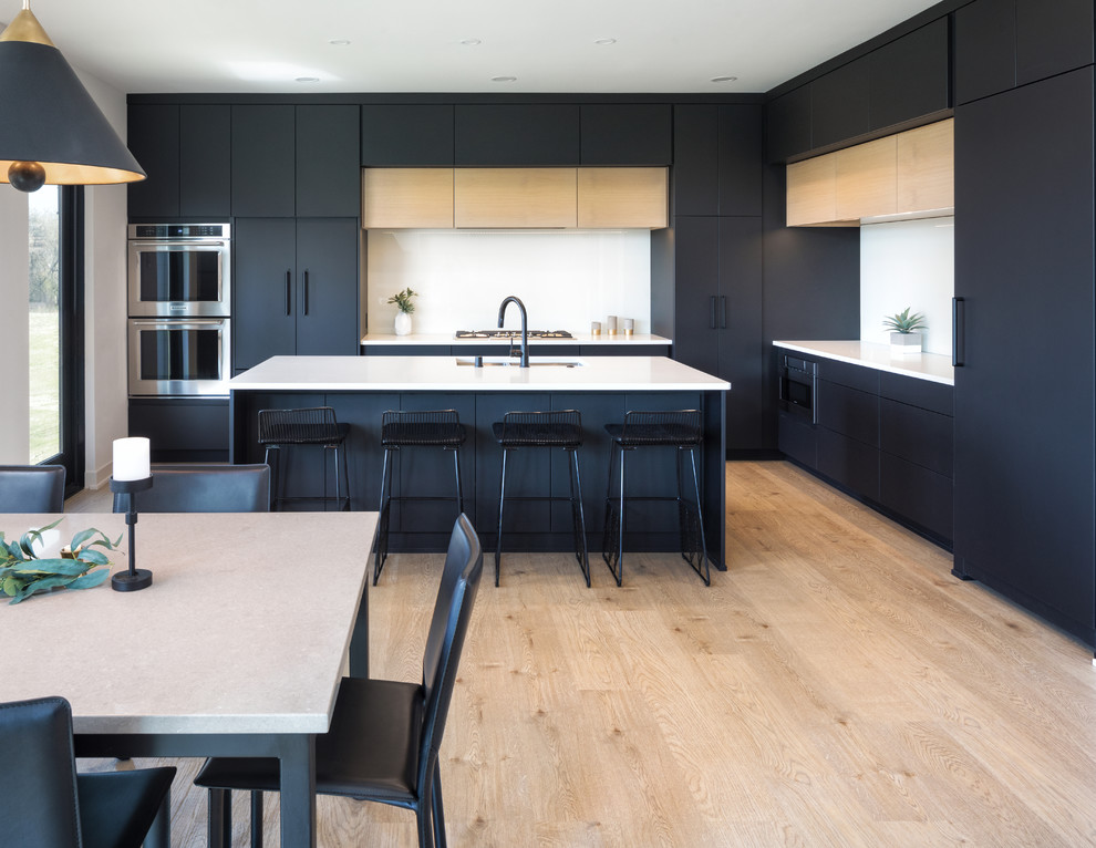 Design ideas for a large contemporary l-shaped open plan kitchen in Minneapolis with a double-bowl sink, flat-panel cabinets, black cabinets, engineered stone countertops, white splashback, glass sheet splashback, black appliances, vinyl flooring, an island, beige floors and white worktops.