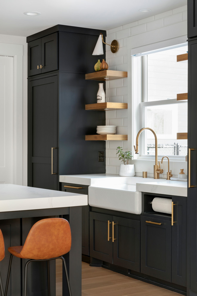 Inspiration for a classic kitchen/diner in Minneapolis with a belfast sink, blue cabinets, engineered stone countertops, white splashback, ceramic splashback, stainless steel appliances, light hardwood flooring, an island, brown floors and white worktops.