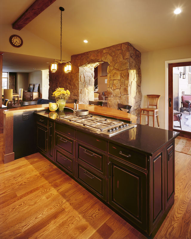 Inspiration for a rustic l-shaped kitchen pantry in Denver with raised-panel cabinets, dark wood cabinets, composite countertops, light hardwood flooring, an island, black splashback, stone tiled splashback and stainless steel appliances.